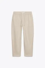 Pantalón color beige de tiro medio con cintura elástica ajustable con cordones, bolsillos delanteros y falsos bolsillos de vivo en la espalda. El bajo es ajustable con botón a presión.