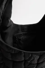 Bolso de hombro negro fabricado en tejido técnico acolchado con diseño geométrico. Tiene un compartimento principal con cierre mediante imán, un bolsillo plano y un bolsillo con cierre mediante cremallera en el interior.