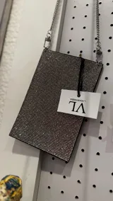 Cartera rectangular porta celular con superficie cubierta de brillos plateados y correa de cadena metálica.