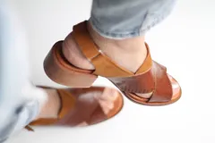 Sandalias de cuero marrón con tiras cruzadas en el empeine y tira alrededor del tobillo.