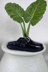 Zuecos cerrados de cuero marrón oscuro, con puntera redonda y tira ancha con hebilla metálica y ojales.