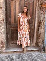 Vestido largo con estampado abstracto en tonos camel, naranja y blanco, con escote en V, mangas cortas con volados y falda con volados en el ruedo.