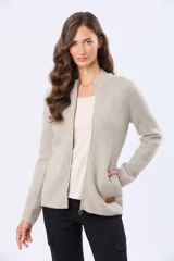 Campera tejida color beige, con cierre frontal, cuello alto y bolsillos laterales. Presenta una textura abrigada y un parche decorativo de cuero sintético en el bolsillo izquierdo.