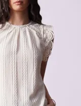 Blusa color crema en tejido elastizado, con aplique de puntilla en las sisas y abertura con botón en la espalda.