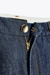 Pantalón de jean azul oscuro, corte wide leg, tiro alto con pinzas delanteras, bolsillos laterales y cierre frontal con cremallera y botón.