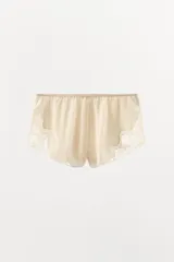 Shorts tipo lencero color crema confeccionado en tejido satinado con tiro alto, cintura elástica y detalle de encaje a tono en el ruedo.