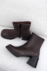 Botín de cuero marrón oscuro, con punta cuadrada, cierre lateral y taco ancho y geométrico. Presenta una plataforma delantera.