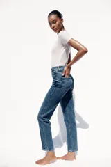 Pantalón de jean gris oscuro, de corte mom fit, tiro alto y largo tobillero. Cuenta con cinco bolsillos, cierre frontal con cremallera y botón.