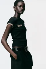 Camiseta negra de corte slim fit, cuello redondo y manga corta. Presenta falsos bolsillos en el delantero y detalle de hilo metalizado en mangas y bolsillos.