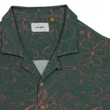 Camisa de manga corta con cuello resort en color verde oscuro, con un estampado de líneas abstractas y flores en color rosado. Presenta cierre frontal de botones y un calce relajado.