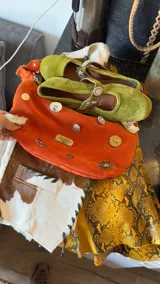 Cartera baguette color celeste con rayas verticales blancas, bordados de un sol y un caballo en la parte superior, y apliques de tachas y dijes en la parte inferior.