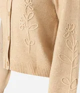 Cardigan de punto color beige, con cuello redondo, cierre frontal de botones, mangas largas con puños acanalados y bordado floral en las mangas y el frente.
