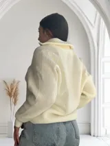 Sweater de punto color crudo con cuello polo y cierre metálico.