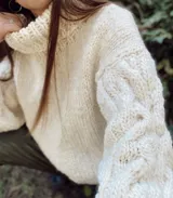 Sweater tejido a mano color crudo, de lana merino virgen sin teñir, con cuello alto y mangas largas con diseño trenzado.
