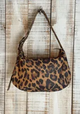 Bolso de hombro color blanco con textura craquelada, correa regulable con hebilla, interior forrado y cierre superior. Incluye llavero y bolsillos internos.