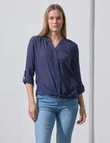 Blusa blanca de gasa marca Zac & Rachel, con cuello a la base, escote en V, abertura central con botones, bolsillo aplicado en el pecho y mangas largas regulables con presilla y botón. Tiene terminación opcional de nudo en el ruedo.