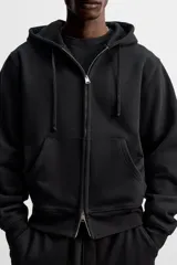 Sudadera negra relaxed fit de algodón compacto con interior en rizo, cuello con capucha ajustable, manga larga, bolsillos frontales tipo canguro, acabados en rib y cierre frontal con cremallera.