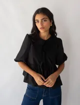 Blusa negra de popelina de algodón con corte peplum, mangas abullonadas y lazo en el cuello.