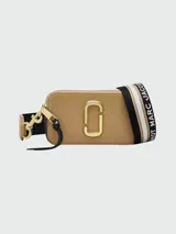 Cartera bandolera Marc Jacobs modelo The Snapshot, color marrón claro con logo dorado y correa ancha de tela con la inscripción "The Snapshot Marc Jacobs" en blanco y negro.