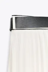 Falda midi color blanco, de tiro alto y corte evasé, con plisado vertical y cinturón negro con hebilla dorada.