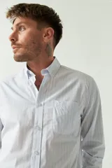 Camisa celeste a rayas rojas de hombre, manga larga, con bolsillo y logo bordado.