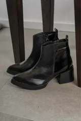 Bota corta de cuero marrón con puntera redondeada y taco cuadrado. Presenta una correa con hebilla alrededor del tobillo y cierre lateral.