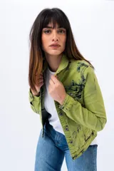 Campera de jean verde con efecto tie dye en negro, corte clásico, cuello camisero, cierre frontal con botones metálicos y bolsillos con solapa en el pecho.