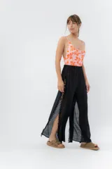 Pantalón negro de gasa liviana con cintura elástica y aberturas laterales terminadas en detalle de pompones.