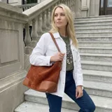 Bolso tipo hobo o bucket bag de eco cuero con textura símil gamuza color marrón óxido. Presenta detalles de costura en contraste en la base, que es de cuero liso color caramelo. Tiene una correa de hombro ajustable.