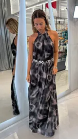 Vestido largo estampado en tonos negro, gris y rosado, con cuello halter drapeado y caída fluida. Se complementa con un cinturón metálico de eslabones circulares.