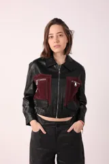 Campera corta de cuero sintético negra con detalles en gamuza color borgoña en la parte superior del pecho y bolsillos con cierre.