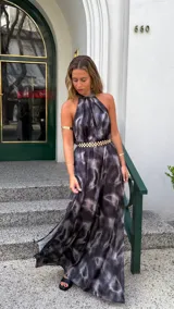 Vestido largo con estampado tie-dye en tonos grises y negros, con cuello halter y espalda descubierta. Incluye cinturón dorado con eslabones y abertura lateral.