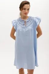 Vestido corto celeste de lino, corte suelto, con cuello redondo con volados y lazo, mangas cortas con volados.