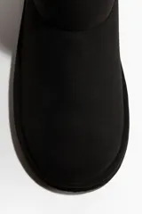 Botas cortas negras con forro interior de tejido suave efecto peludito y suela acanalada. Presentan costuras decorativas y una trabilla en la parte trasera del tobillo.