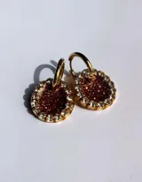 Par de aros colgantes con dije circular de resina con glitter multicolor y borde de strass. El arito es de acero quirúrgico dorado.