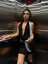 Conjunto de top halter y minifalda, ambos de lentejuelas negras. El top es corto y tiene un escote pronunciado. La falda es ajustada y de tiro alto.