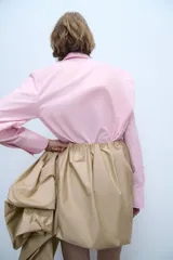 Camisa de popelín rosa de algodón, con cuello solapa, manga larga con puños plisados y volumen en un hombro. Cierre frontal con botones ocultos.