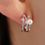 Aros tipo argolla plateados con tres aros paralelos, con incrustaciones de strass y una perla.
