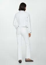 Chaqueta de jean blanca con cuello camisero, cierre frontal con botones negros, bolsillos de parche en el pecho y mangas largas con puños abotonados.