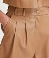 Bermuda color camel de material sintético, con cintura alta, trabillas, cierre con cremallera y botón, bolsillos laterales, pliegues frontales y ruedo con dobladillo.