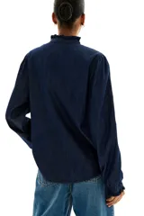 Camisa de denim azul oscuro con cuello mao y volados en cuello y puños. Tiene mangas largas abullonadas con botón en los puños, botonadura frontal y bajo redondeado.