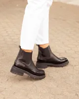 Botas Chelsea negras de cuero, con suela track y detalles de charol en la puntera y el talón.