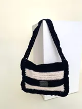 Cartera tejida a crochet en color negro y blanco, con diseño a rayas y volados en los bordes.