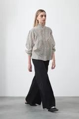 Camisa de viscosa blanca con estampa de lunares negros. Presenta cuello alto con volado y botonadura frontal, mangas largas con puños abullonados y frunces bajo el busto.