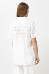 Camisa verde con cuello clásico, manga corta y cierre frontal con botones. Presenta diseño patchwork con detalles de broderie y calados.