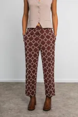 Pantalón marrón chocolate con estampa geométrica en tonos crudo, de tiro medio, corte recto, con bolsillos laterales y cintura con elástico en la parte trasera.