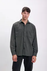 Camisa de hombre color verde oscuro de pana con cuello clásico, cierre frontal con botones, dos bolsillos de parche en el pecho y mangas largas con puños abotonados.