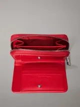 Billetera de piel sintética roja con cierre perimetral de cremallera y logo metálico de Calvin Klein en el frente. Posee 8 ranuras para tarjetas, billetero y bolsillo monedero con cremallera.