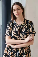 Vestido camisero midi con volados, estampado con hojas en tonos camel, blanco y negro. Tiene cuello redondo, mangas cortas y cierre frontal con botones.