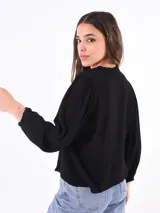 Camisa negra con cuello bebé, manga larga abullonada y cierre frontal con botones.